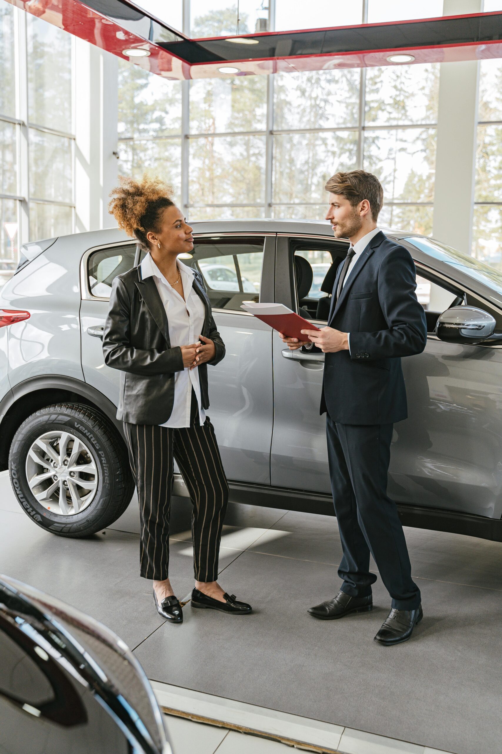 An interaction between a woman and a salesman at a car dealership, discussing vehicle options.