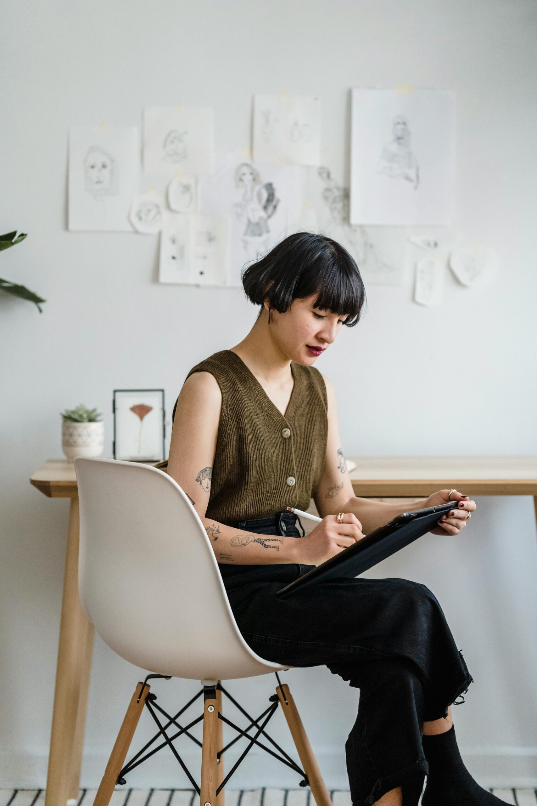 A young woman artist sketching on a tablet in a modern office setting, surrounded by artwork. Creative and focused atmosphere.